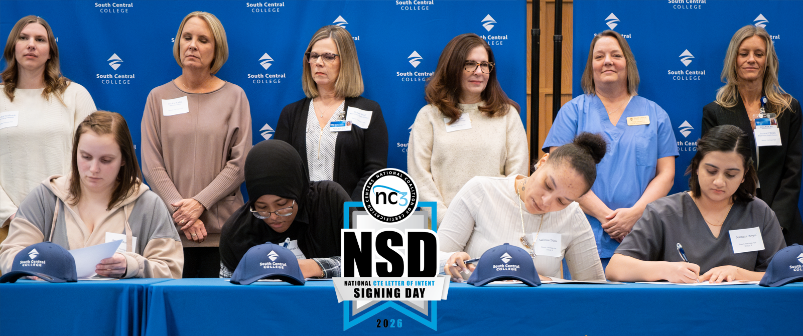 2025 Signing Day students sitting at a table signing documents with faculty overlooking at SCC's Conference Center.