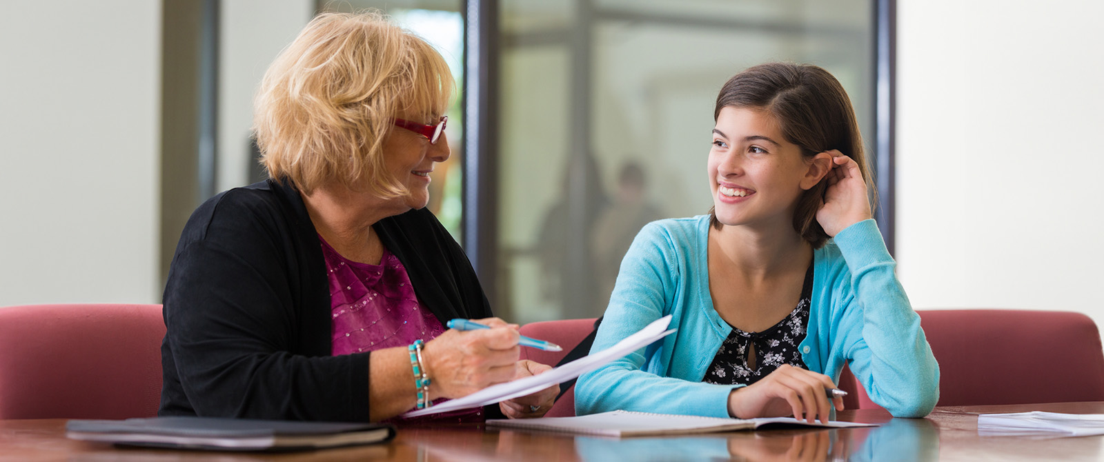 Young woman sitting in a meeting room reviewing paper work with and older woman.