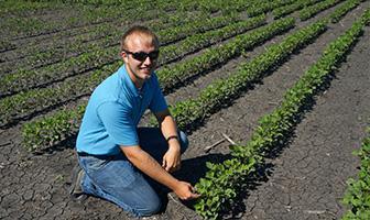 student standing in field with crops growing in the early season