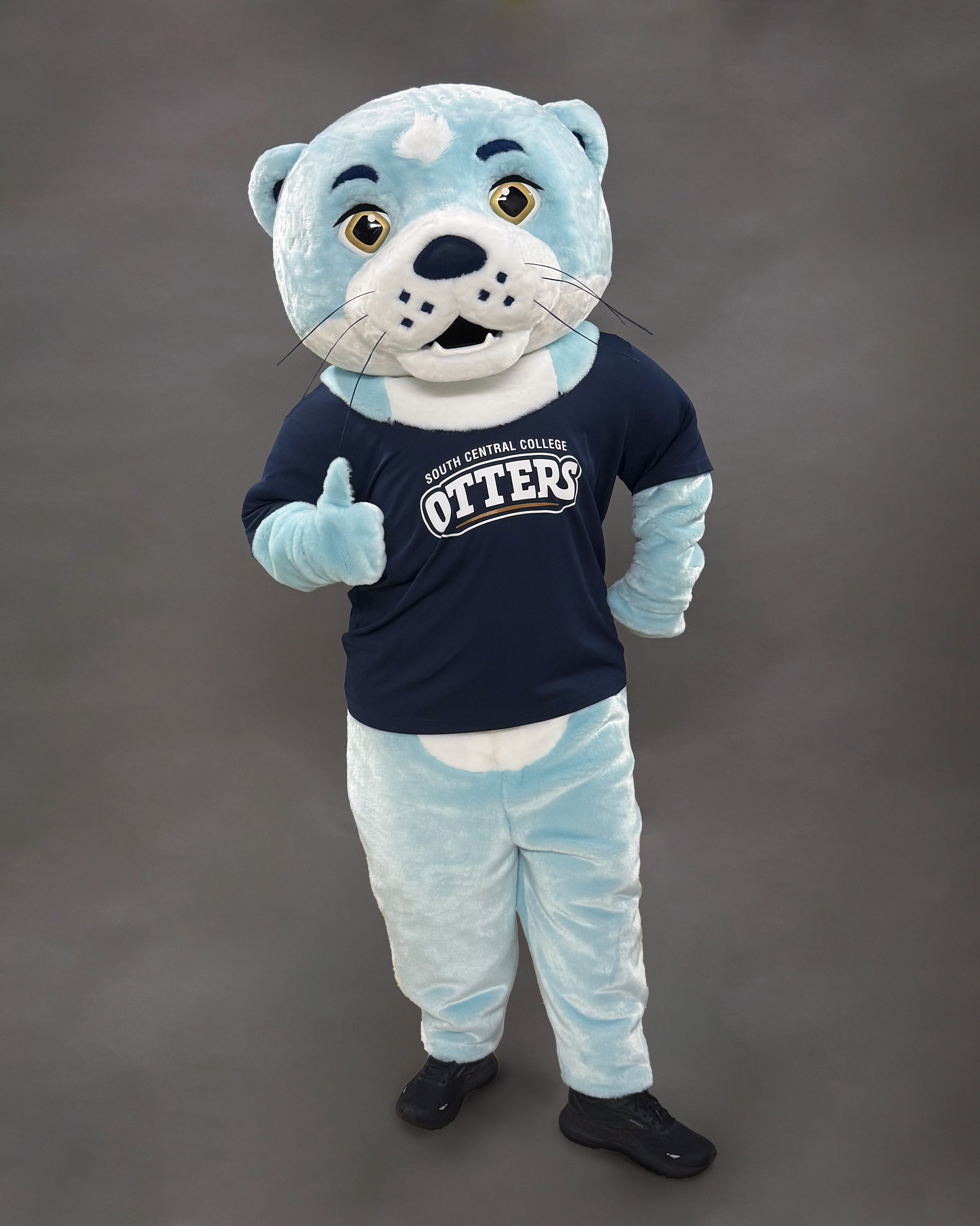 The South Central College otter mascot giving a thumbs-up in a navy &ldquo;Otters&rdquo; T-shirt.