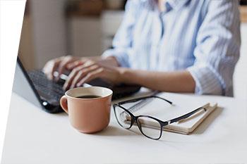 photo of student typing on laptop with coffee and notepad near by