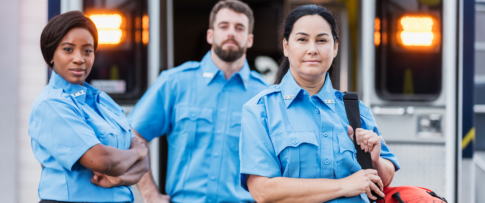 EMTs standing in front of an ambulance looking sternly at the camera