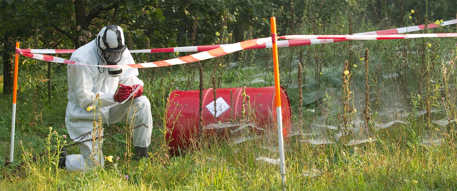Man kneeling at a hazardous chemical spill taking notes in a notebook.