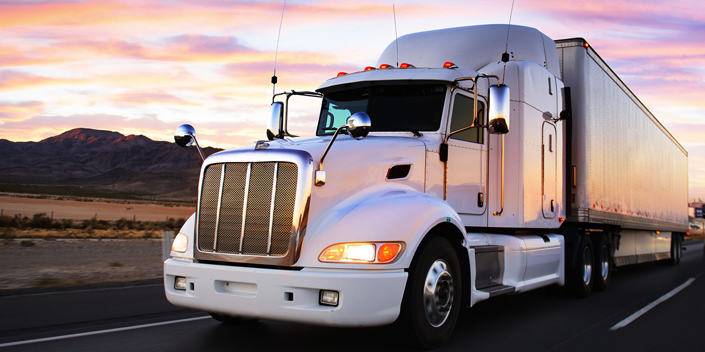 Photo of semi-truck and trailer driving down the road with a golden sunset.
