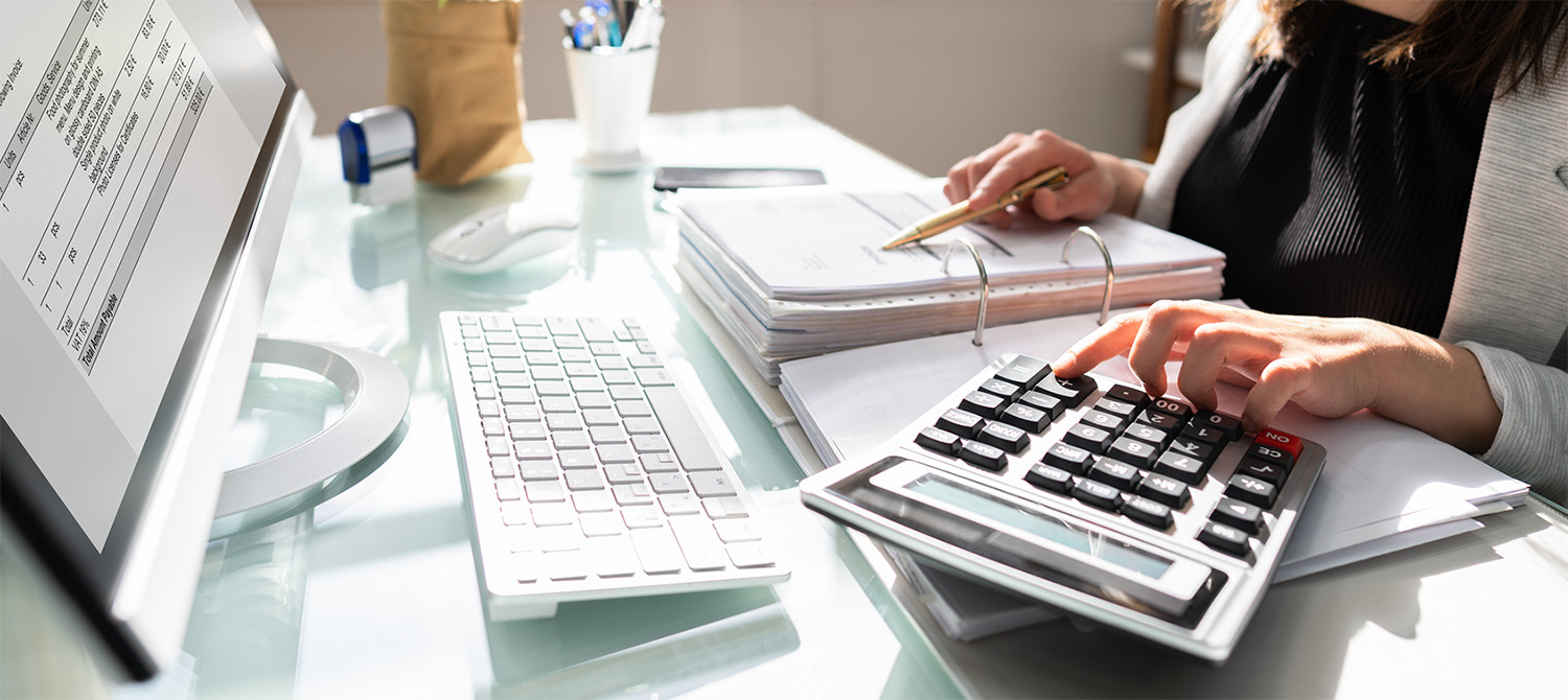 photo of womans hands using calculator and comparing to information in a binder
