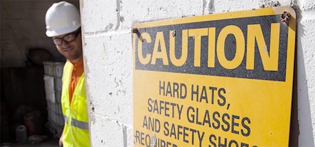 Miner in hard hat looking at caution sign at mining facility