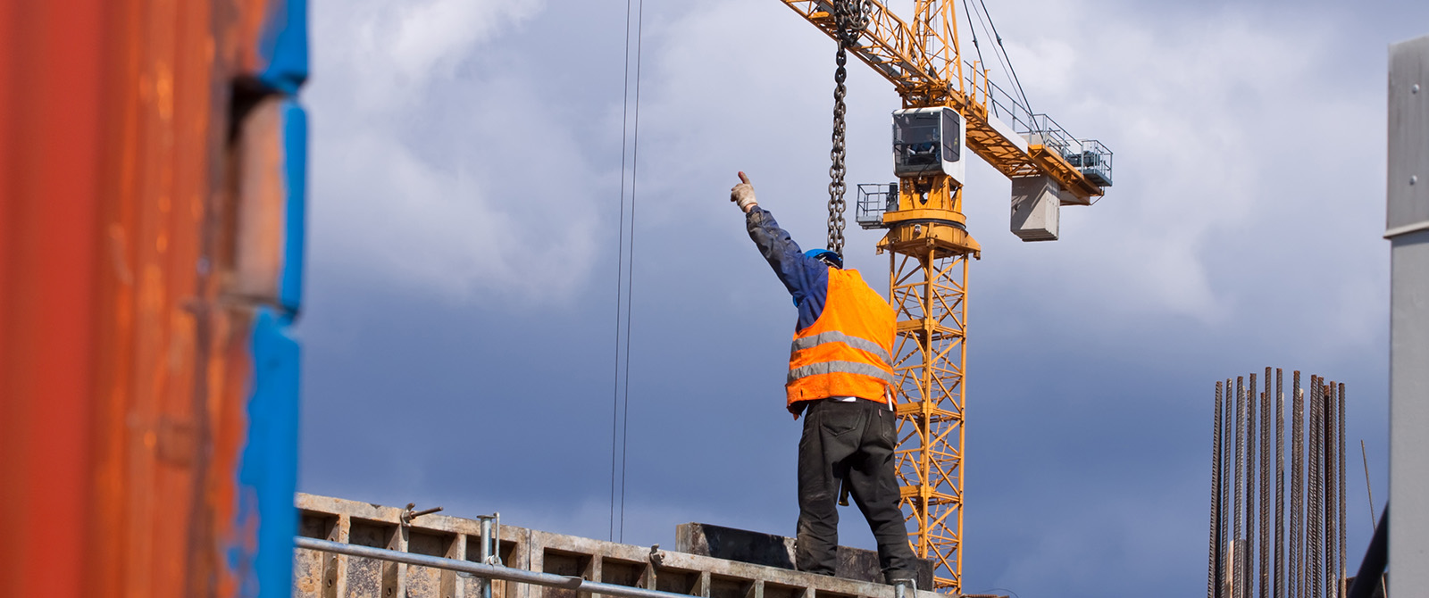 Signalperson pointing toward the sky as a crane lifts a load rigged with chains